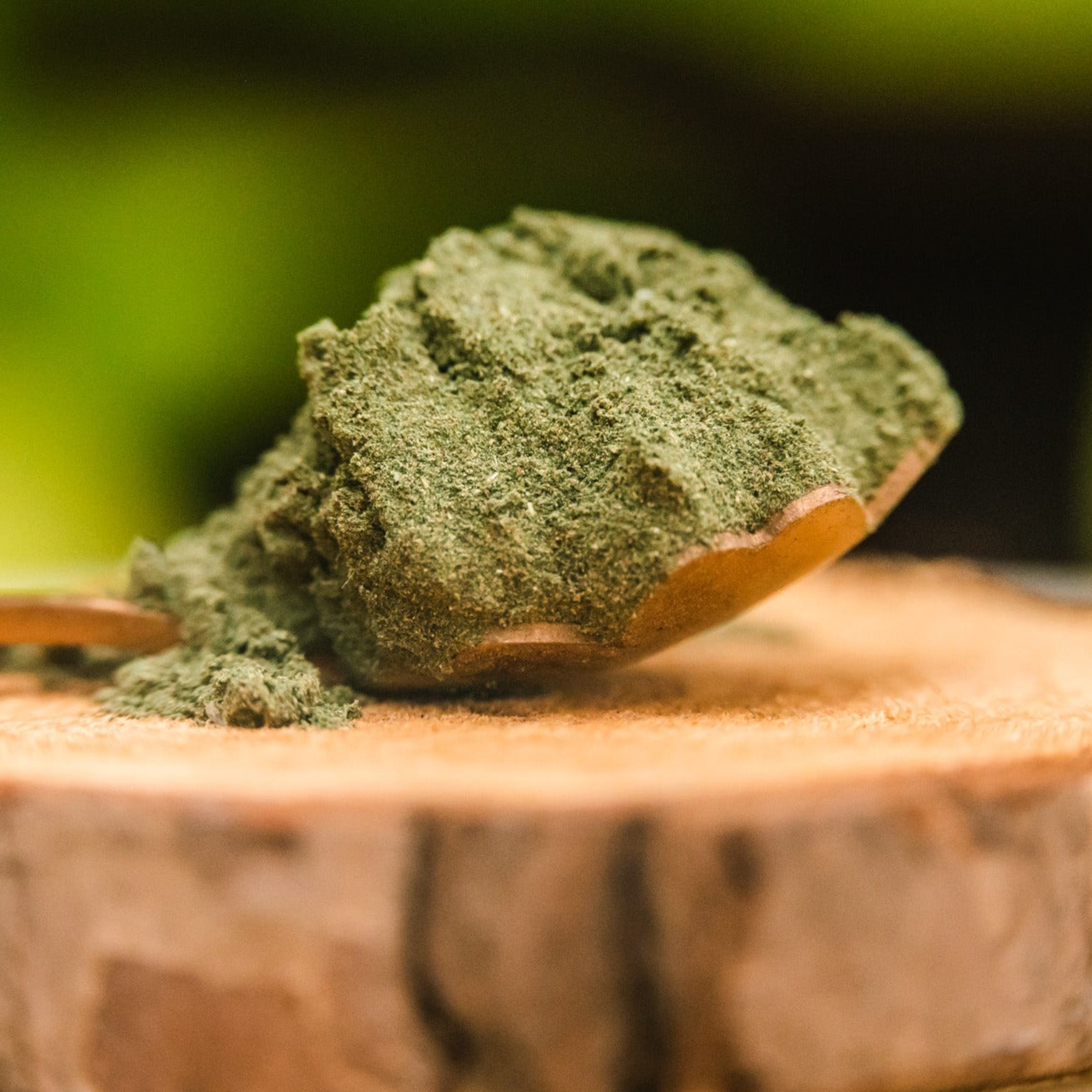 A close up of a gold, flower spoon that is sitting on a piece of wood and holding a spoonful of Fiddy Shades of Green Juice powder.