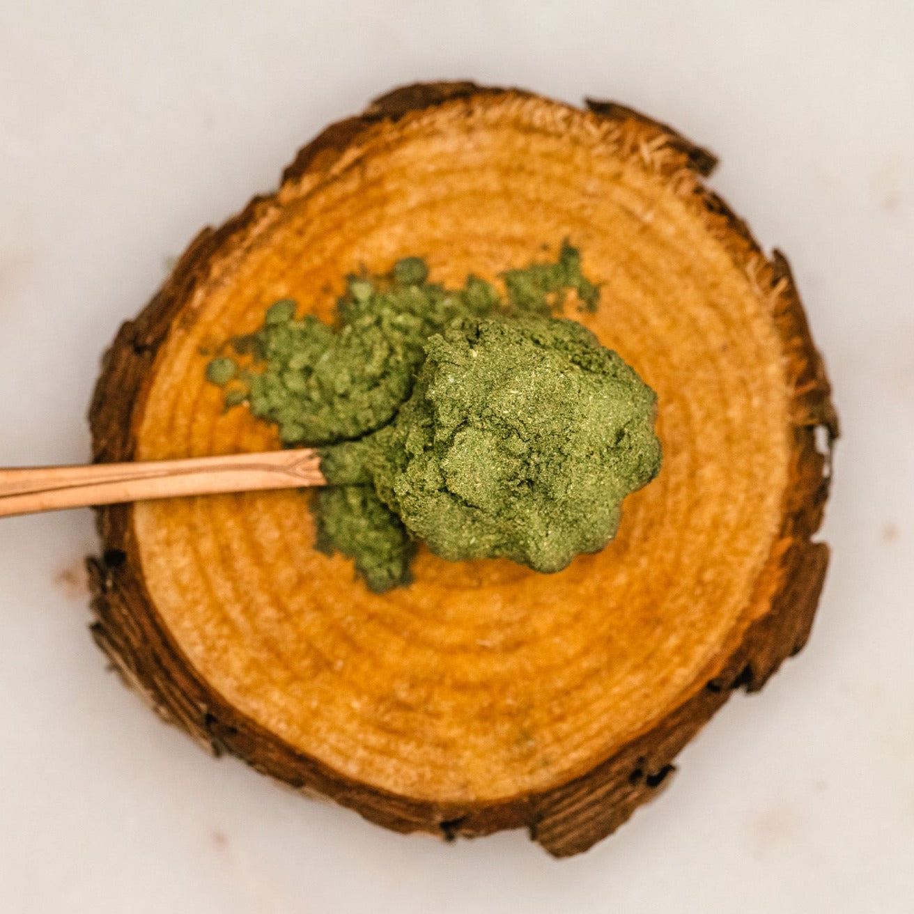 A close up of a gold, flower spoon that is sitting on a piece of wood and holding a spoonful of Fiddy Shades of Green Juice powder.