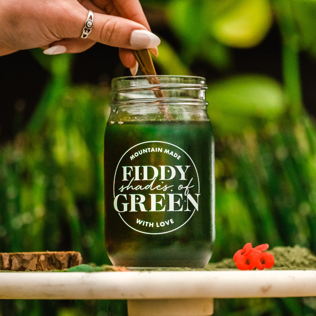 A hand stirring a glass of Fiddy Shades of Green Juice with a gold spoon.